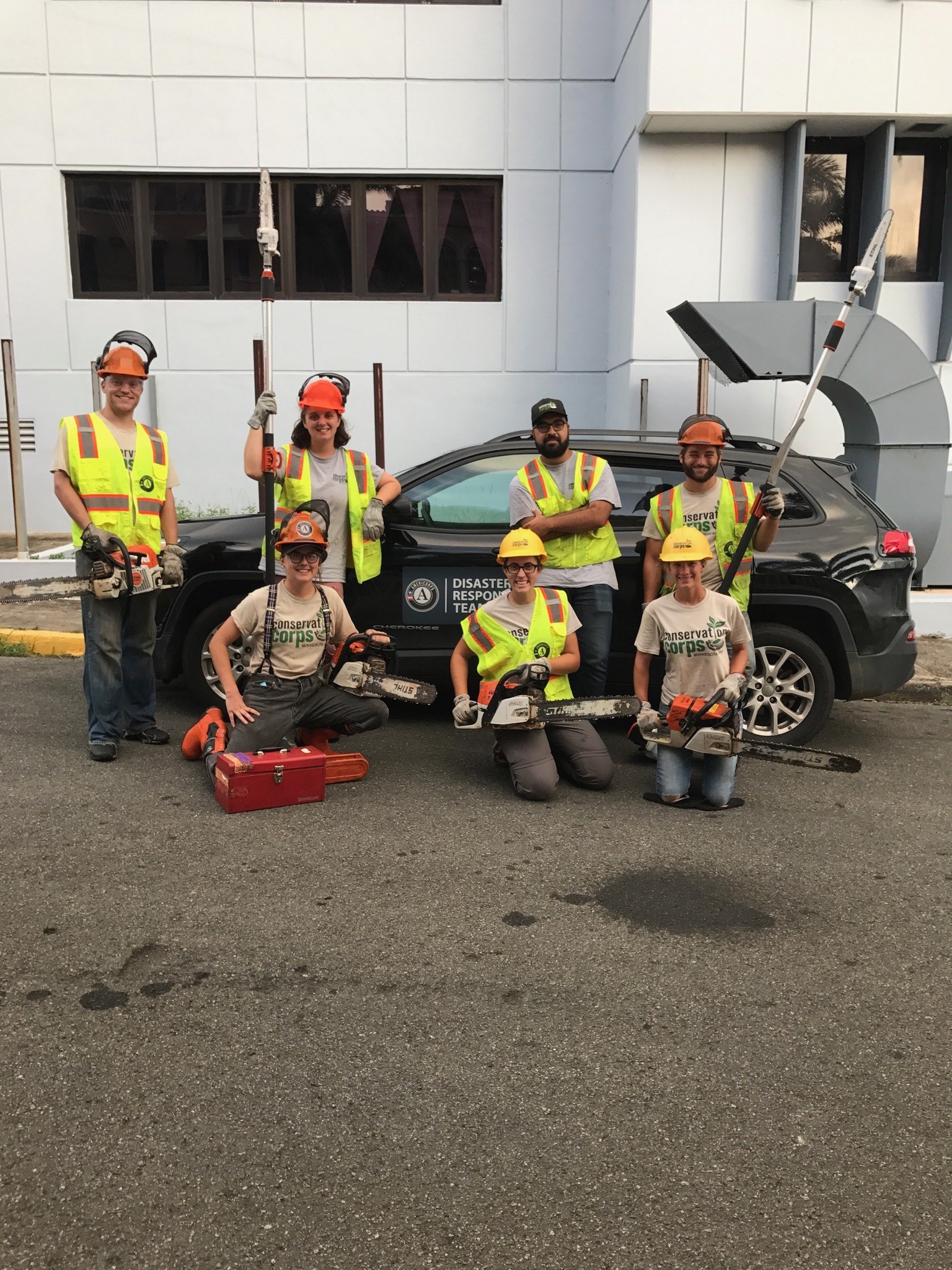 Seven crew members posing in front of black car