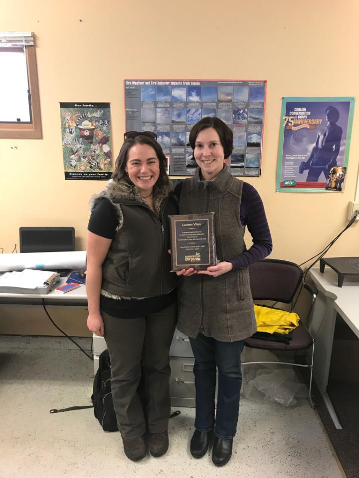 Two people in office with plaque