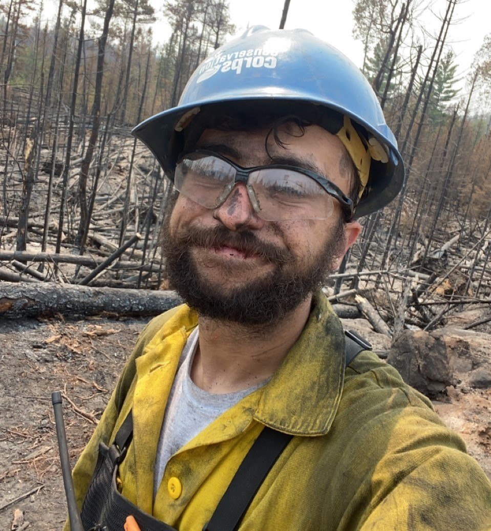 Man in fire fighting gear in a burned forest.