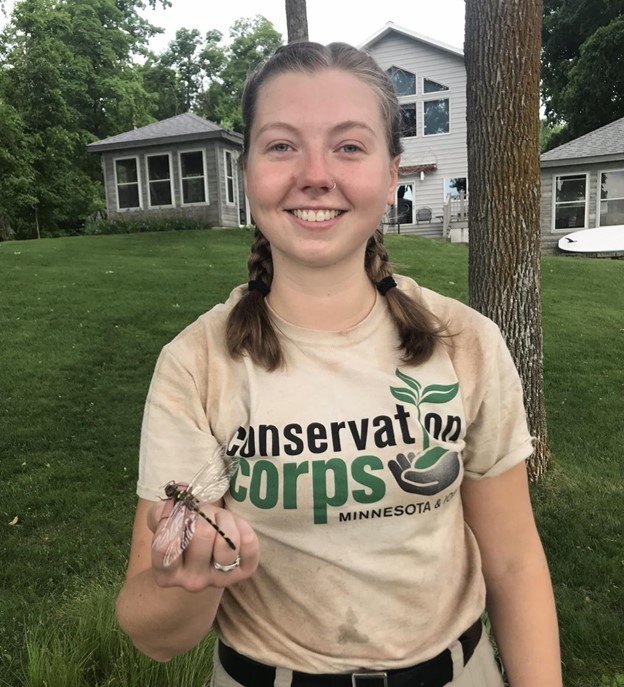 person in corps shirt smiling with dragonfly