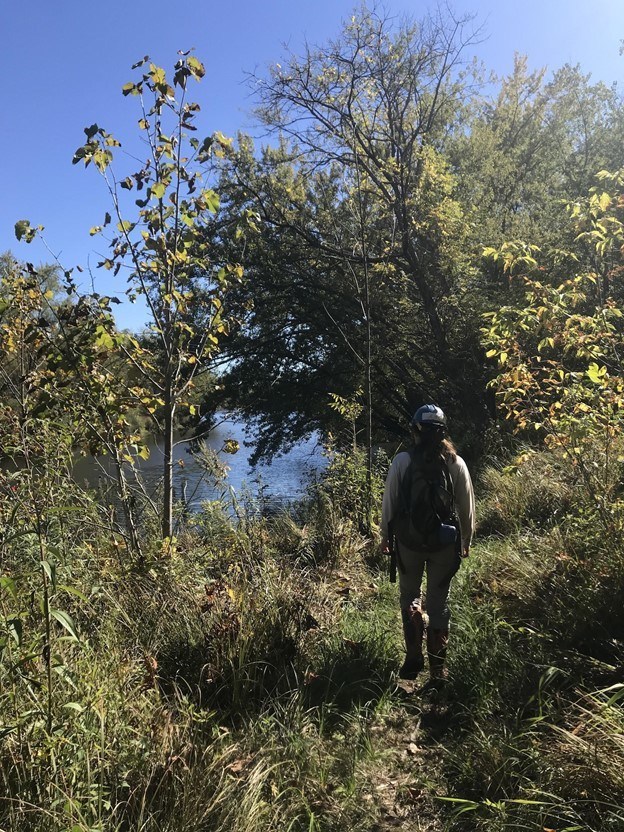 person in helmet walking on trail by river