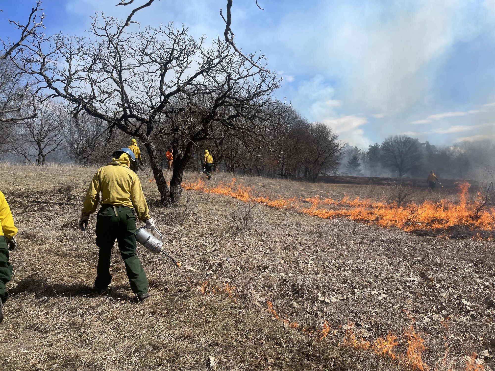 People in fire gear setting fire to grassland