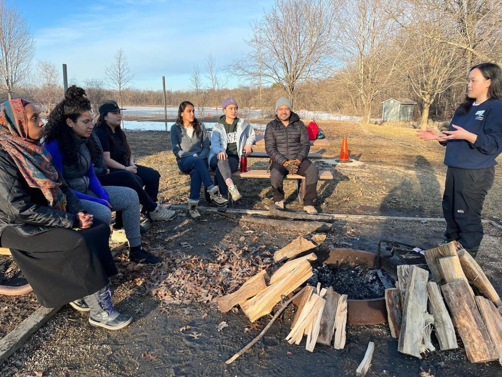 BIPOC Outdoors folks sitting outside on picnic tables listening to Chia