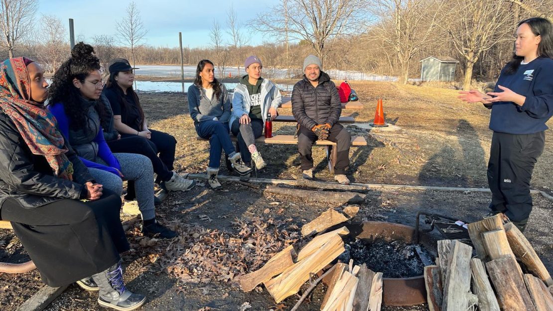 BIPOC Outdoors folks sitting outside on picnic tables listening to Chia