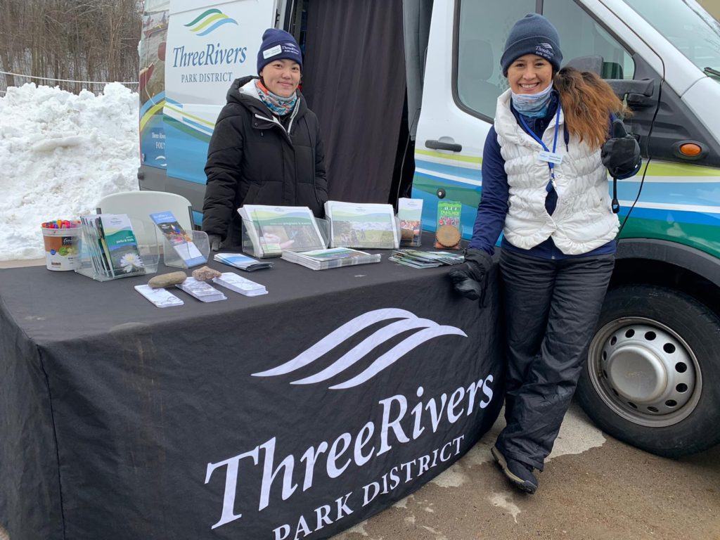 Chia and Giannina standing by Three River table next to van