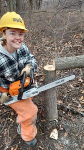 woman posing with chainsaw next to downed tree