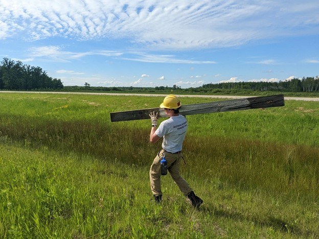 Member carrying wooden beam on shoulder in field