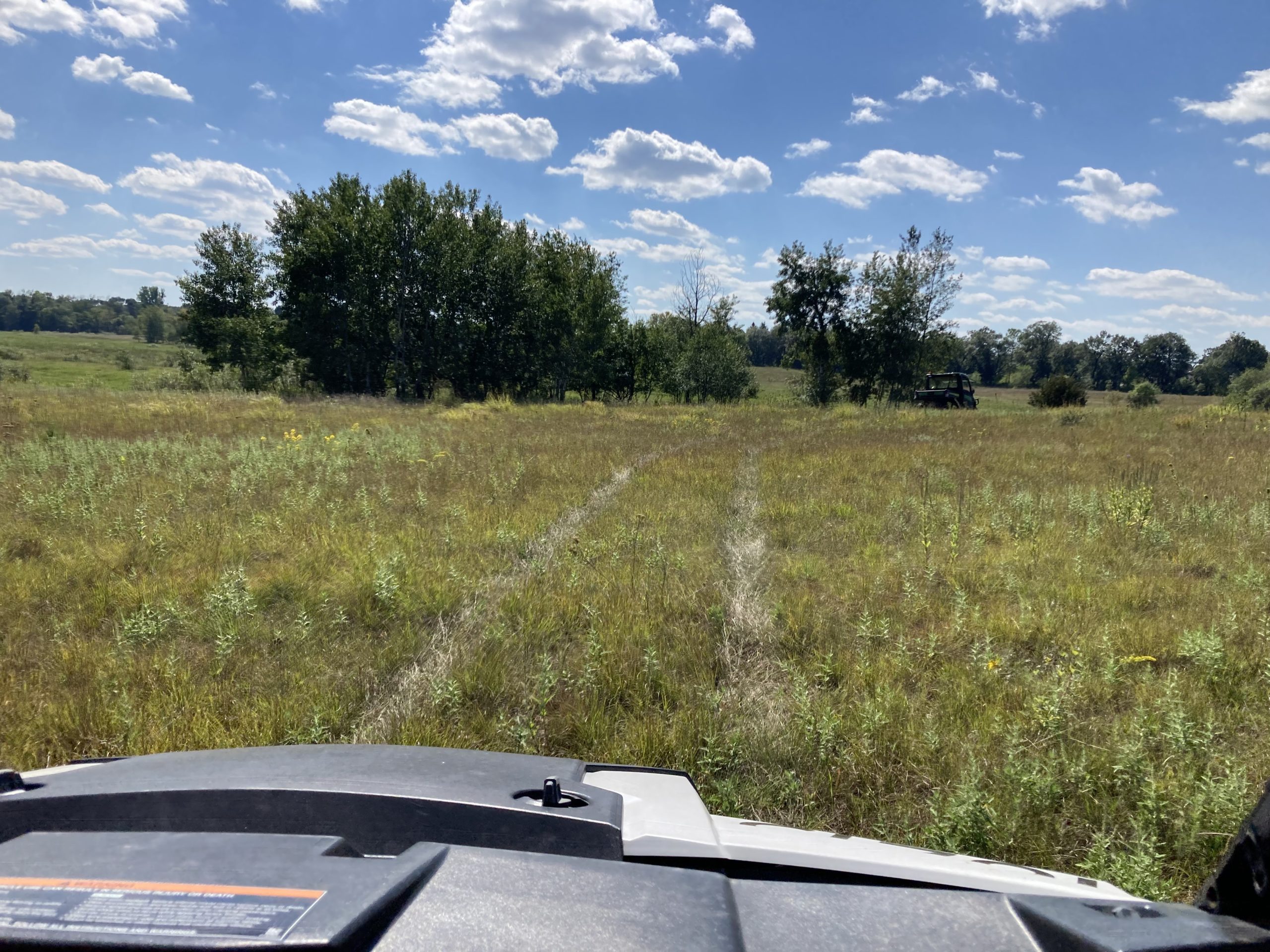 Grassy field with trees in distance viewed from over the hood of an ATV.