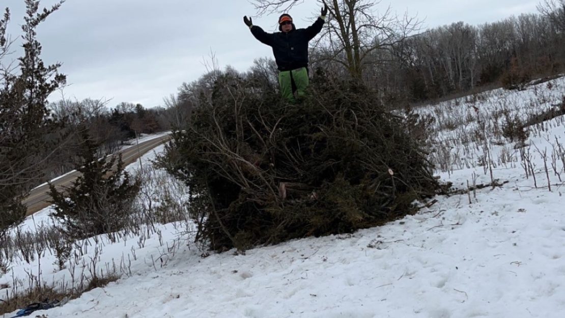 A person sitting on a large brush pile in a snowy field.