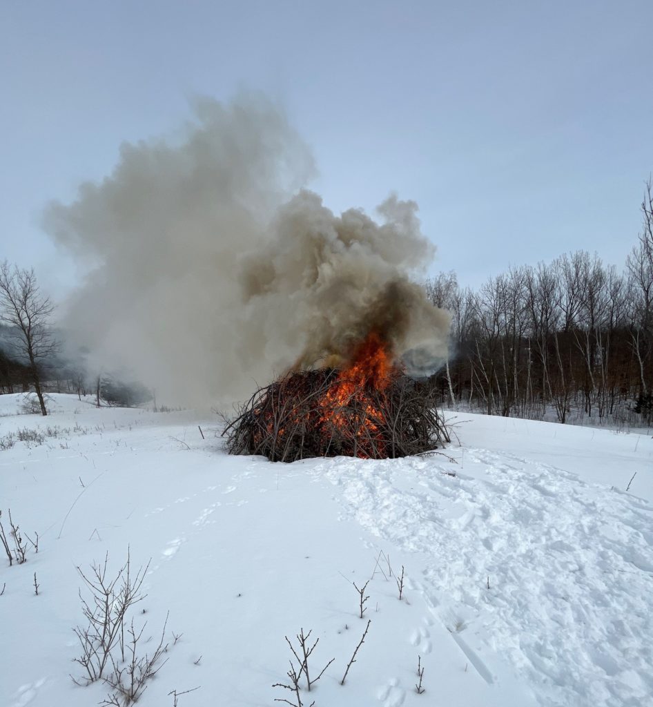 A pile of burning brush in a snowy field.