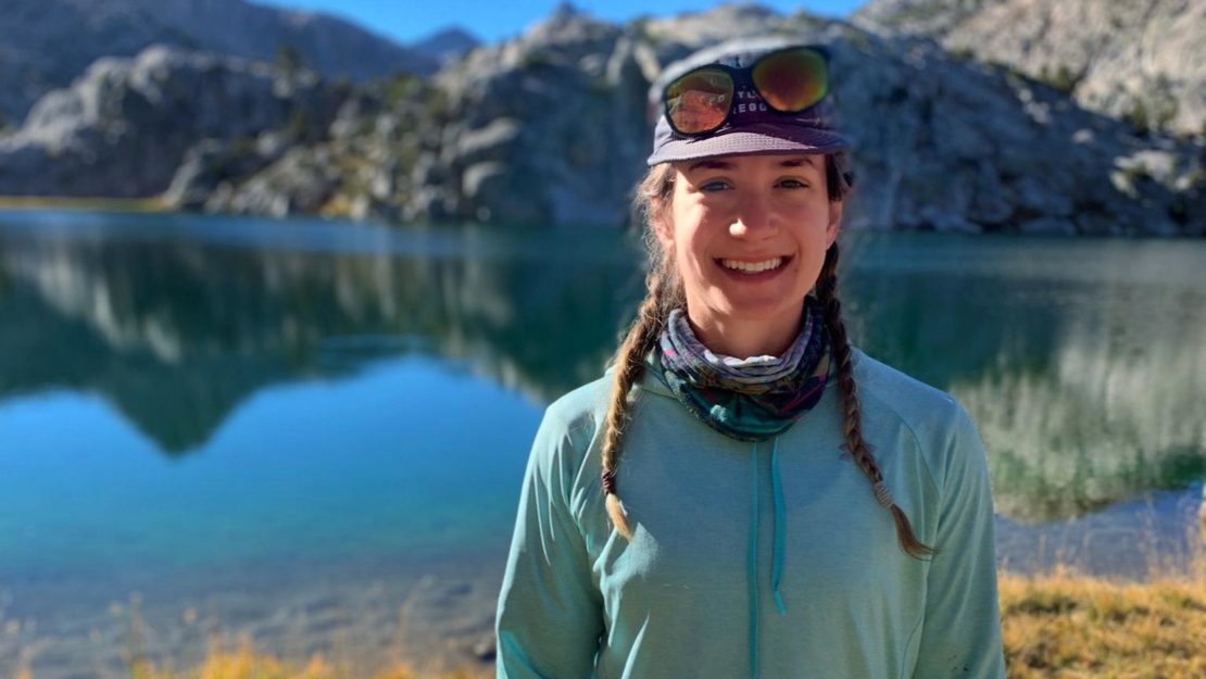 A person smiling in front of a mountain lake.