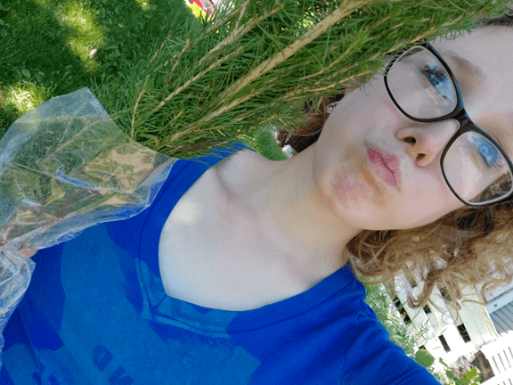 A person taking a selfie holding up a bunch of tree seedlings.