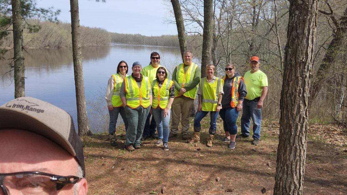 A group of people in high viz vests standing in a campsite by a river.