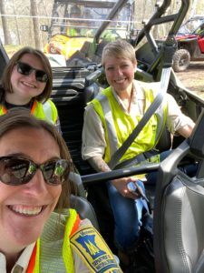 Three people wearing high visibility vests in an ATV