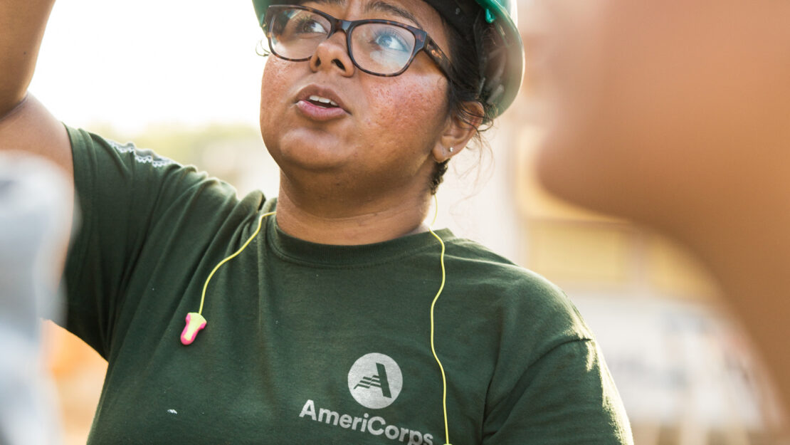 AmeriCorps member in green shirt and hard hat pointing
