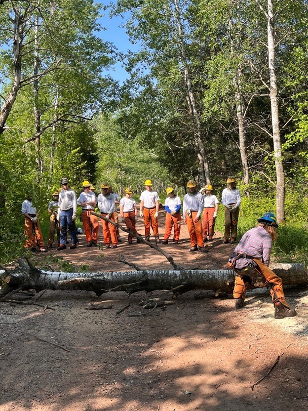 Group of people in Corps gear watching someone how to use a chainsaw.