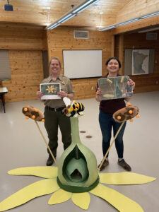 Two people standing behind the completed paper mache flower holding up printed out photos.