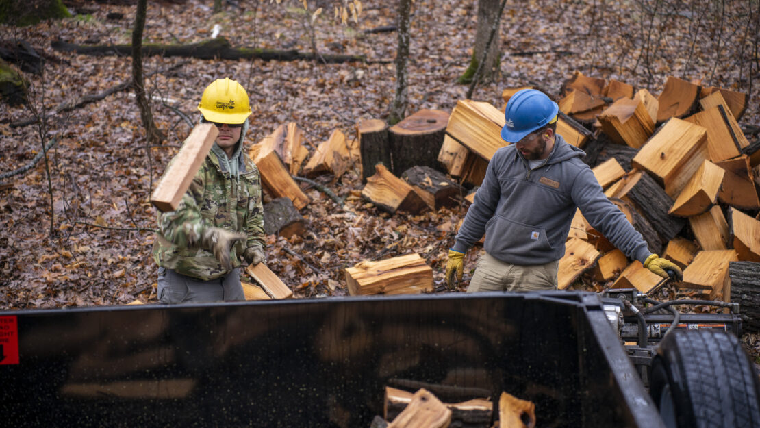 people in Corps helmets throw pieces of firewood into a truck trailer.