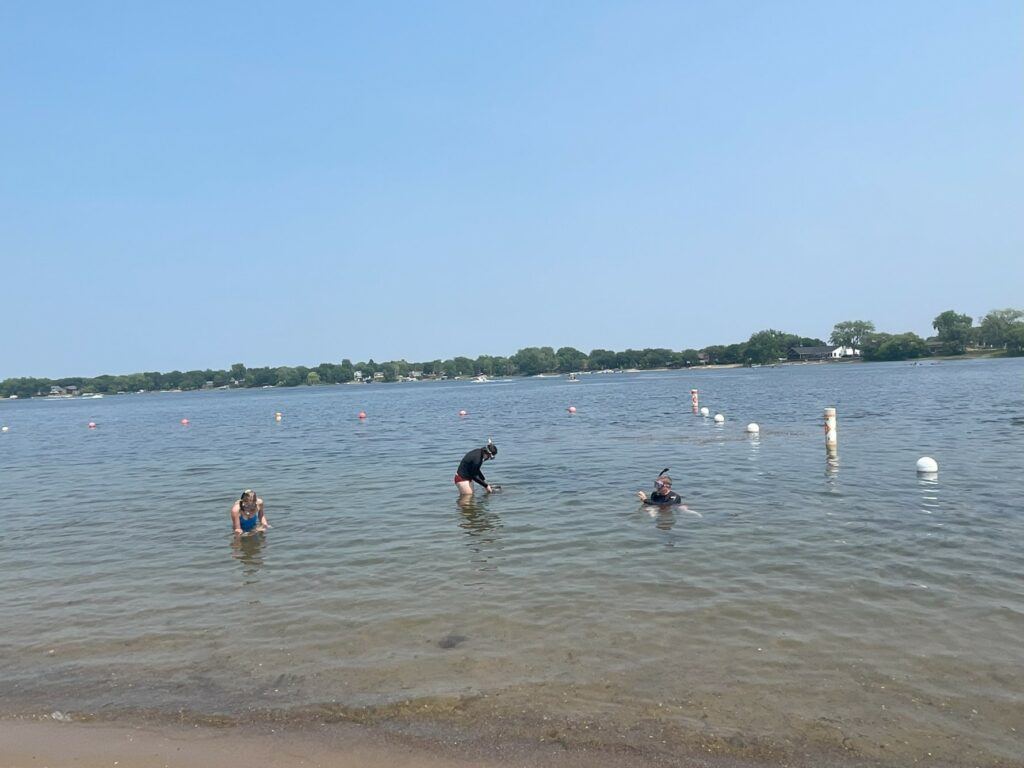 People in swim gear standing in shallow lake water.