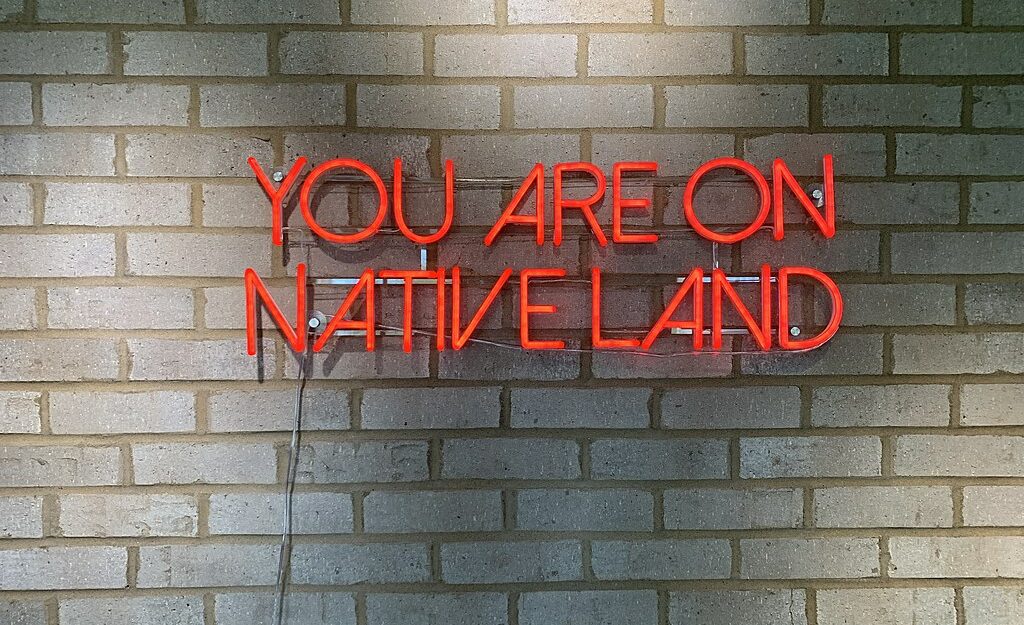A red neon sign that reads “YOU ARE ON NATIVE LAND.”