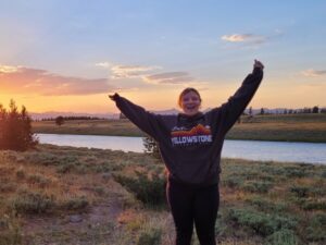 A person wearing a Yellowstone hoody by a river with outstretched arms.