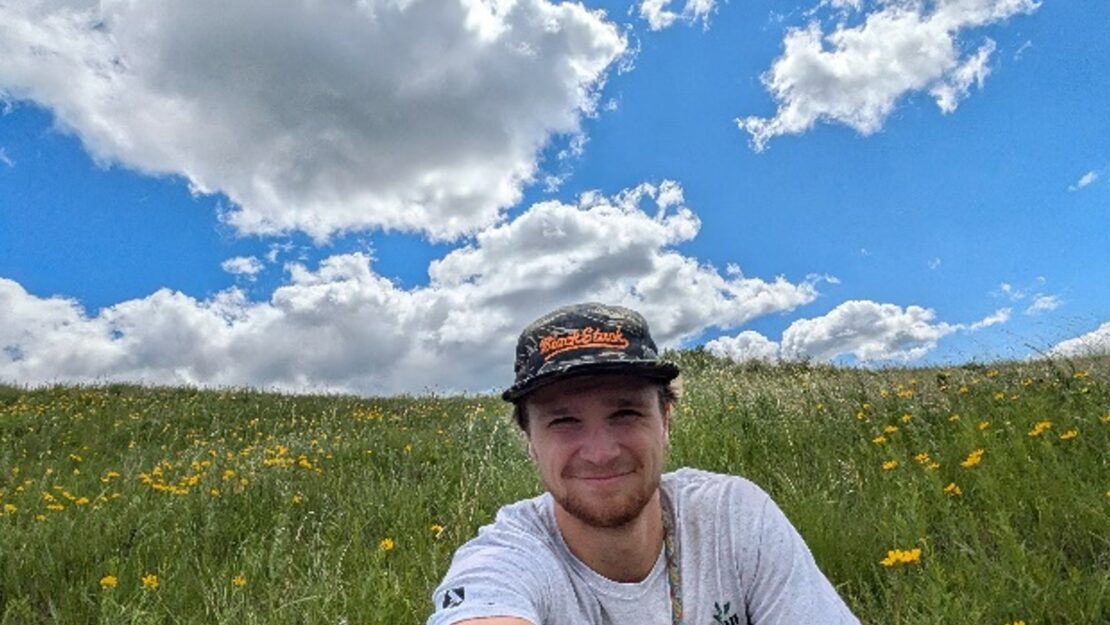 A person in a Corps shirt sitting in a prairie.