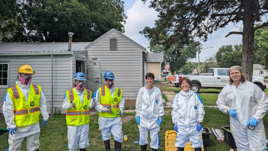 Six people suiting up in head to foot safety gear for mold supression.