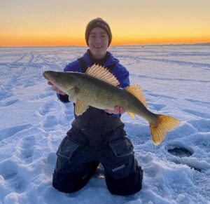 A person in winter gear kneeling on the ice holding a large fish.