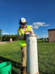 A person in a high visibility vest standing near a tube sticking out of the ground.