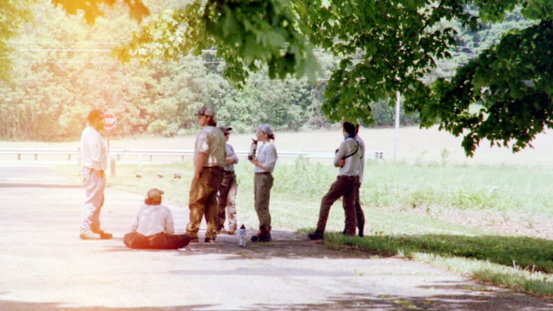 a group of people standing in the shade on a road.