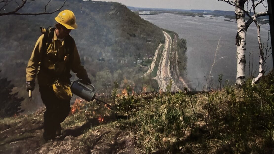 A person in fire gear burning a bluff prairie.