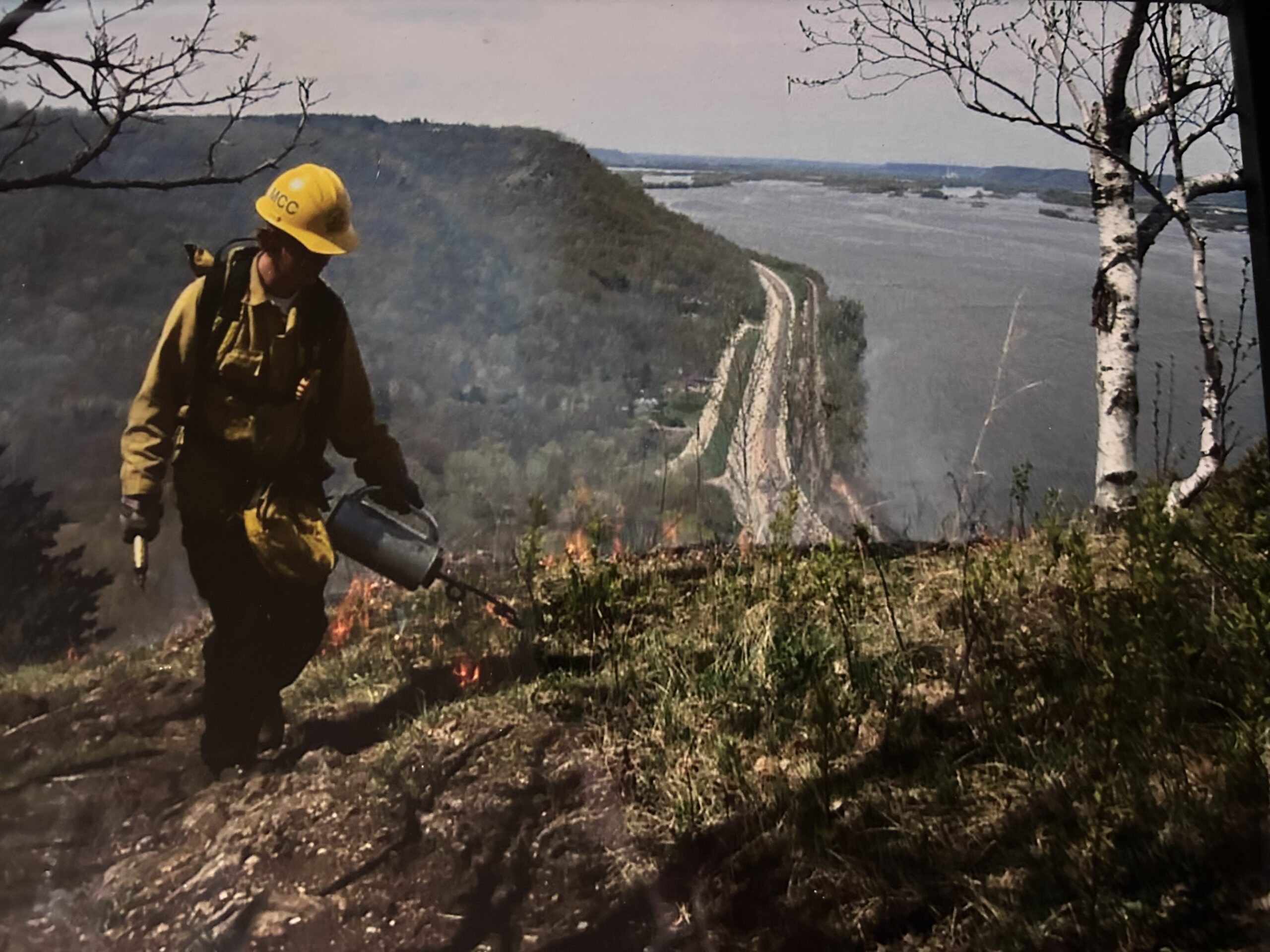 A person in fire gear burning a bluff prairie.