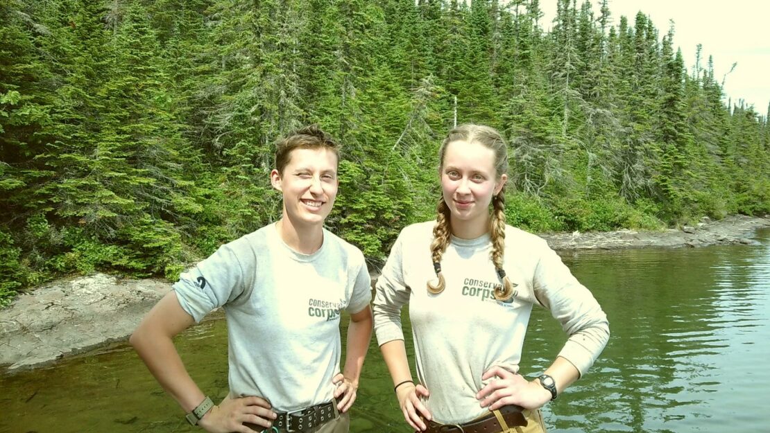 My colead Anna Knutson (left) and I (right) stand next to each other on the tree-lined shore of Lake Superior.