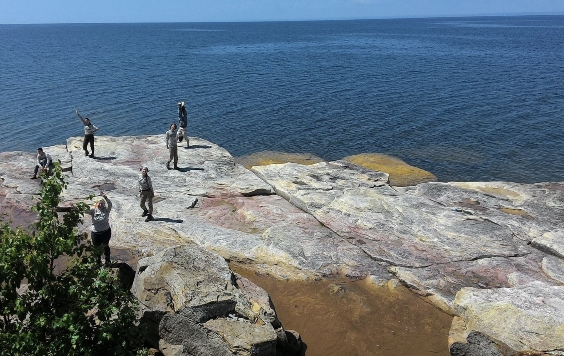 I pose with fellow Youth Members from my 2017 crew for a photo on a large red, gray, and yellow rock formation of the Apostle Islands next to Lake Superior.