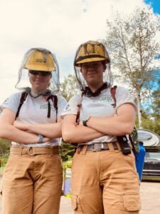 Two people in hard hats look at the camera with crossed arms
