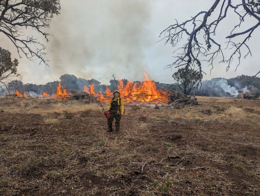 A person in fire gear in front of a prairie fire