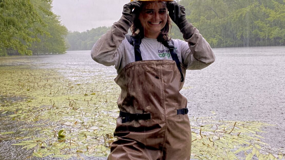 A person in Corps gear in a river while rain drips from her helmet.