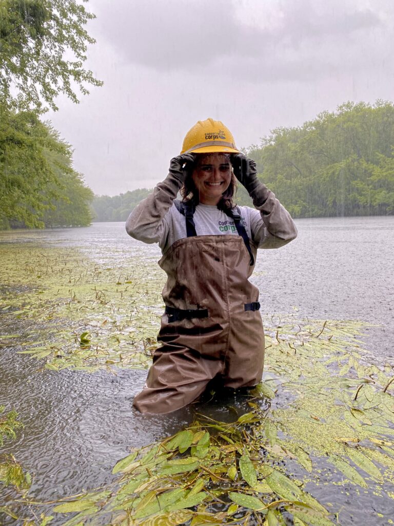 A person in Corps gear in a river while rain drips from her helmet.