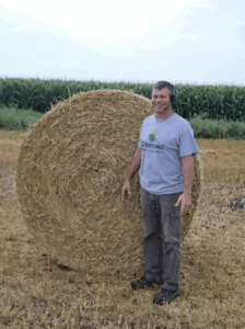 Man standing next to a round hay bale