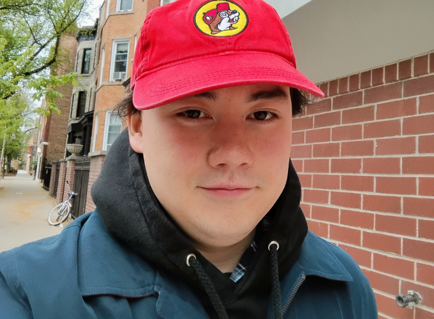 A person wearing a hoodie, blue jacket, and red baseball cap while looking at the camera